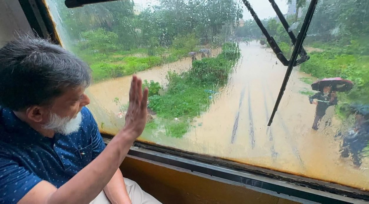 A flooded railway corridor is seen through a rain-streaked train window.