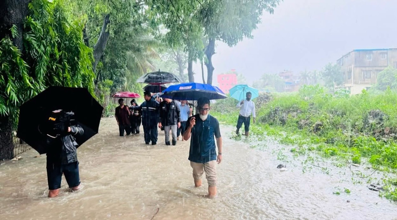 People walk through floodwater and heavy rain beside the submerged Chattogram-Cox's Bazar railway line.