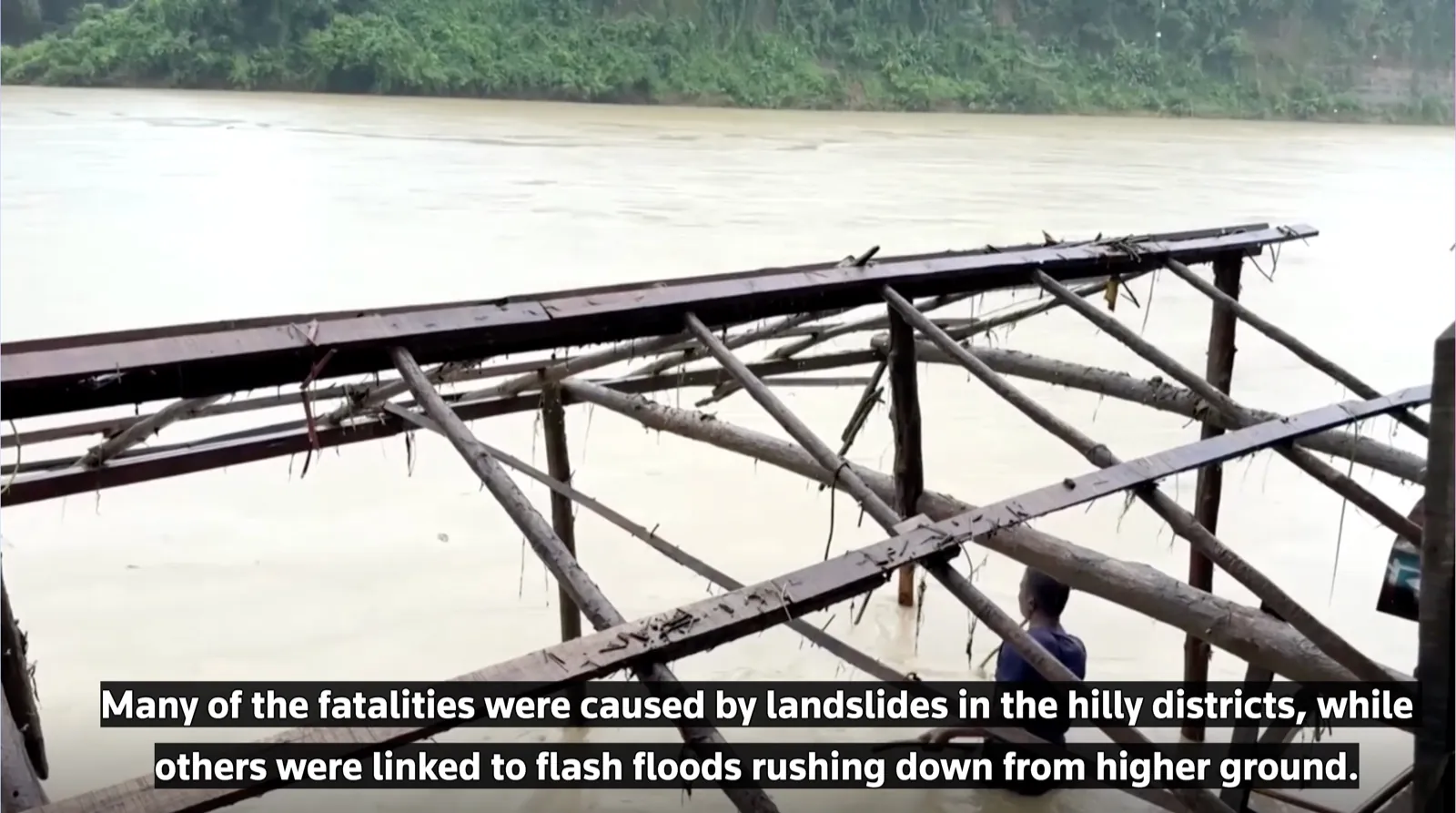 A damaged wooden crossing stands over fast-moving muddy floodwater