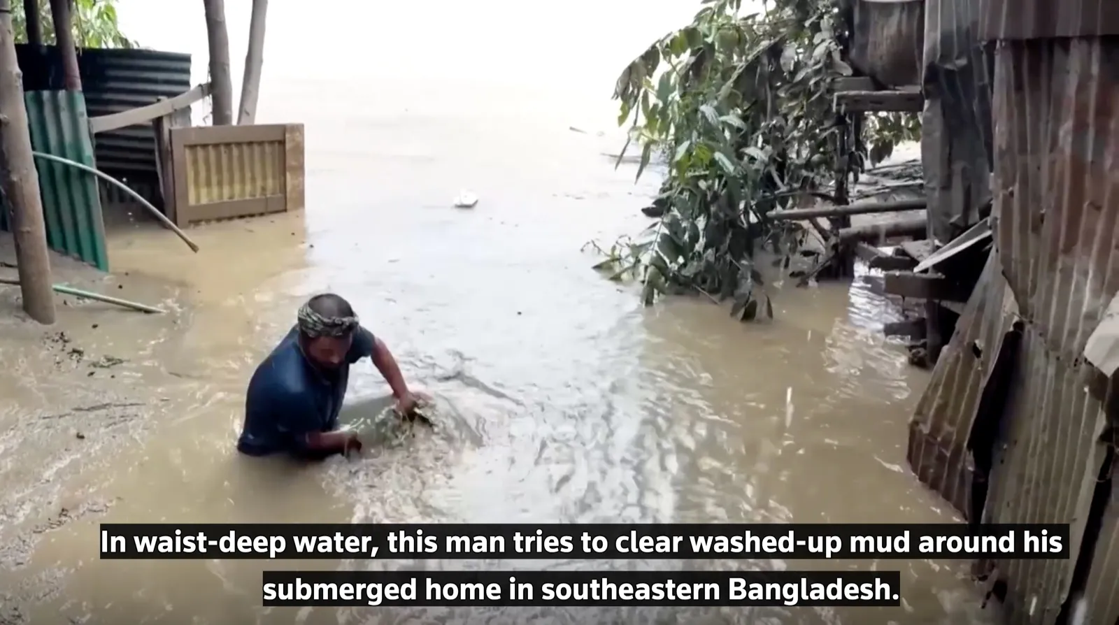 A resident stands waist-deep in floodwater while clearing mud around his submerged home