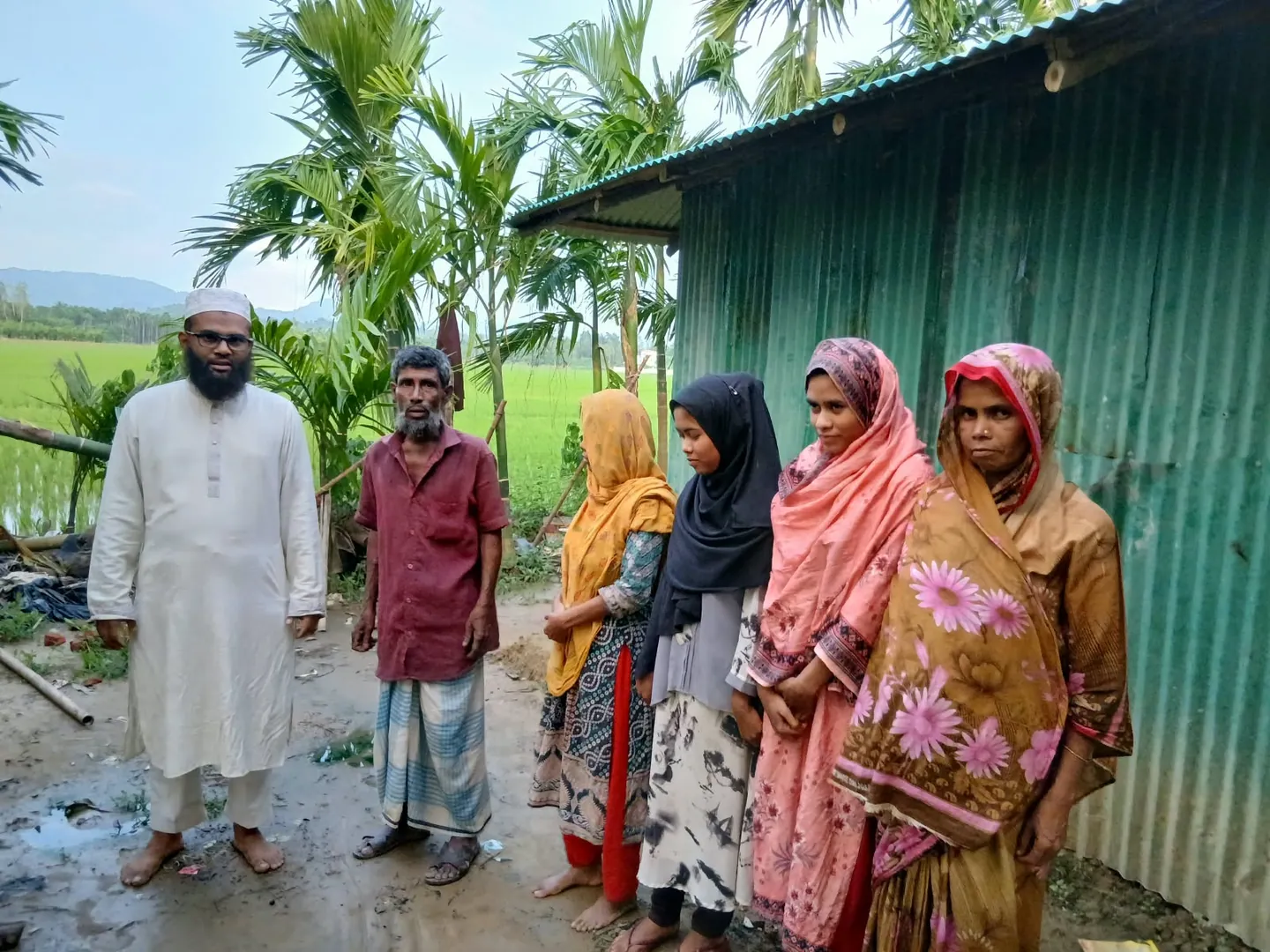 A flood-affected family stands with a Ruhama volunteer outside their home in Bangladesh